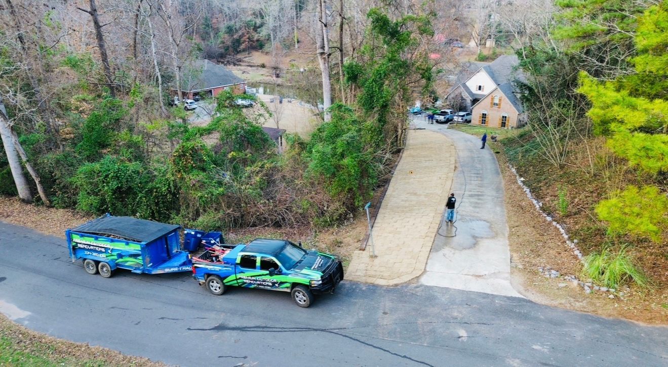 Truck with trailer on a residential road; person standing near a driveway leading to a house.