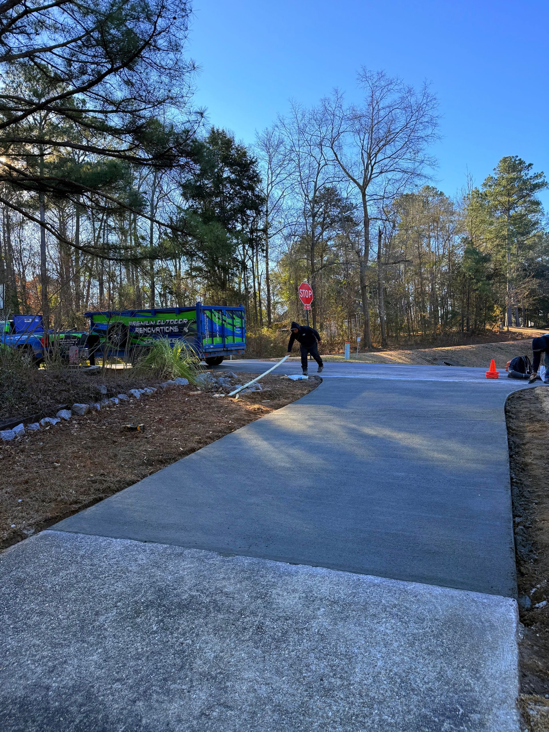 New driveway, with workers near a dumpster and road. Trees and blue sky in the background.