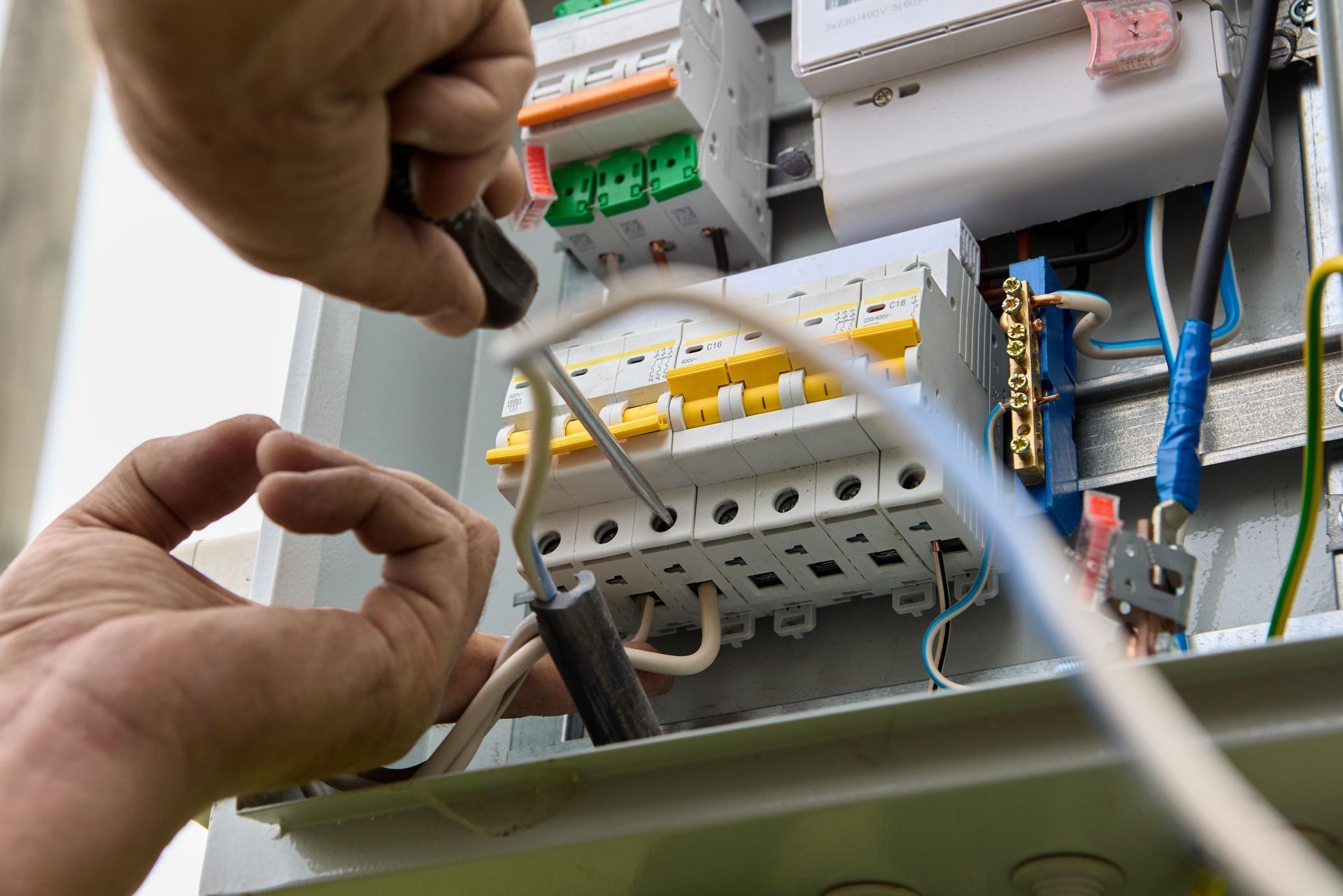 Person using a screwdriver to wire a circuit breaker box with various colored wires.