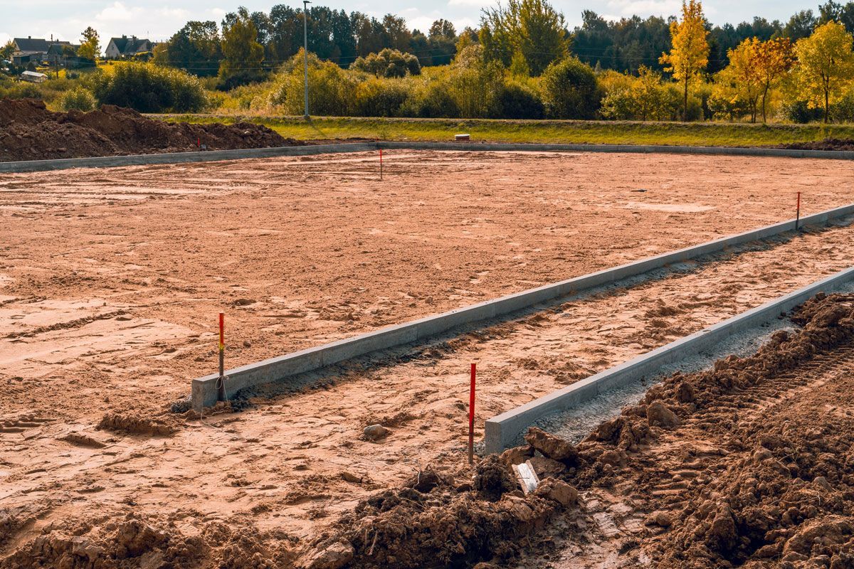 Construction site with cleared land and concrete foundation forms; orange soil and red markers.