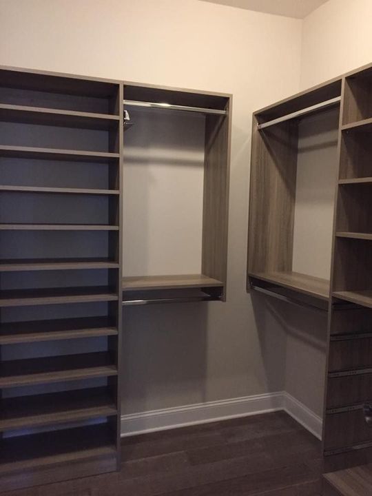 A walk-in closet with wood-finish shelving, a vertical tower of shelves, and hanging rods on light-colored walls.