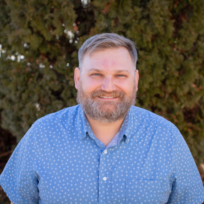 A man with a beard is wearing a blue shirt with white polka dots.