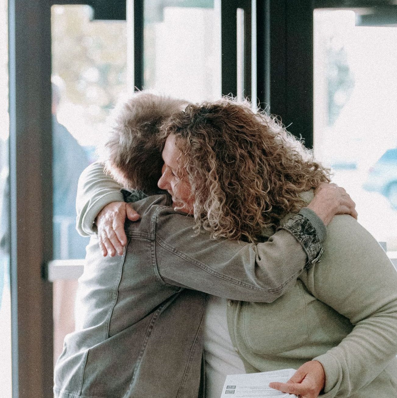Two women are hugging each other in front of a window.