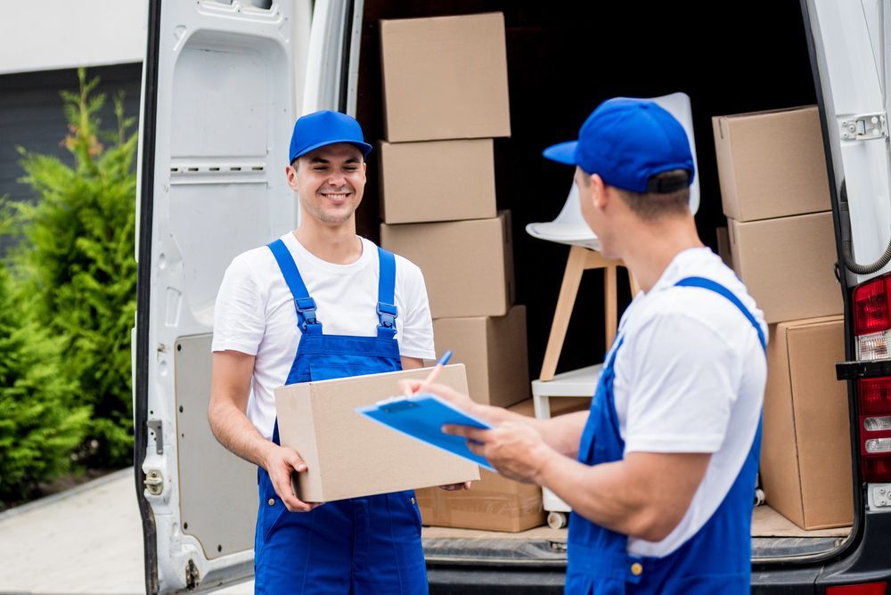 Dos repartidores están parados frente a una camioneta que sostiene cajas.