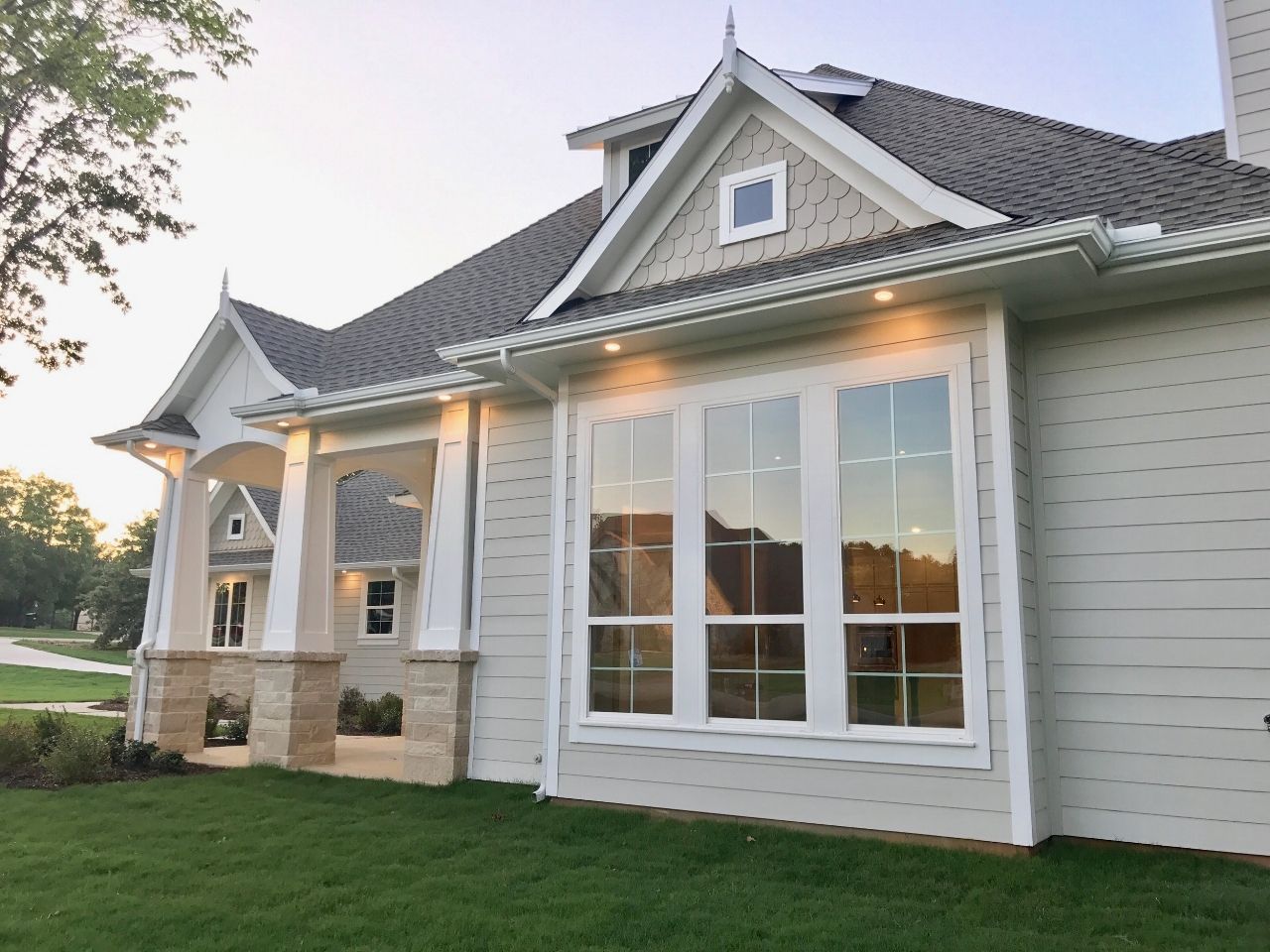 Light gray house exterior with a large bay window, green grass, and trees.