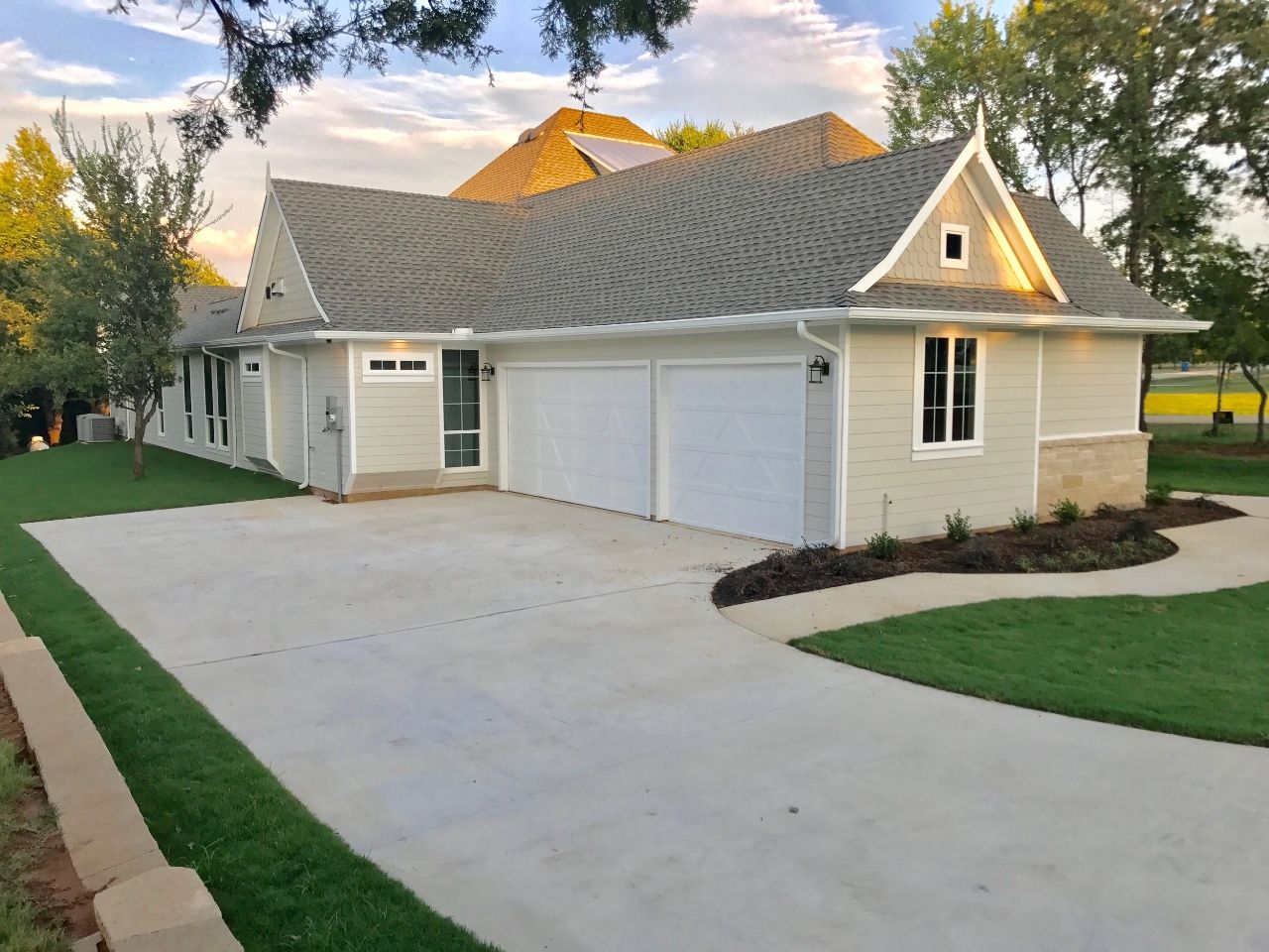 A light-colored house with a driveway and garage, surrounded by grass and trees.