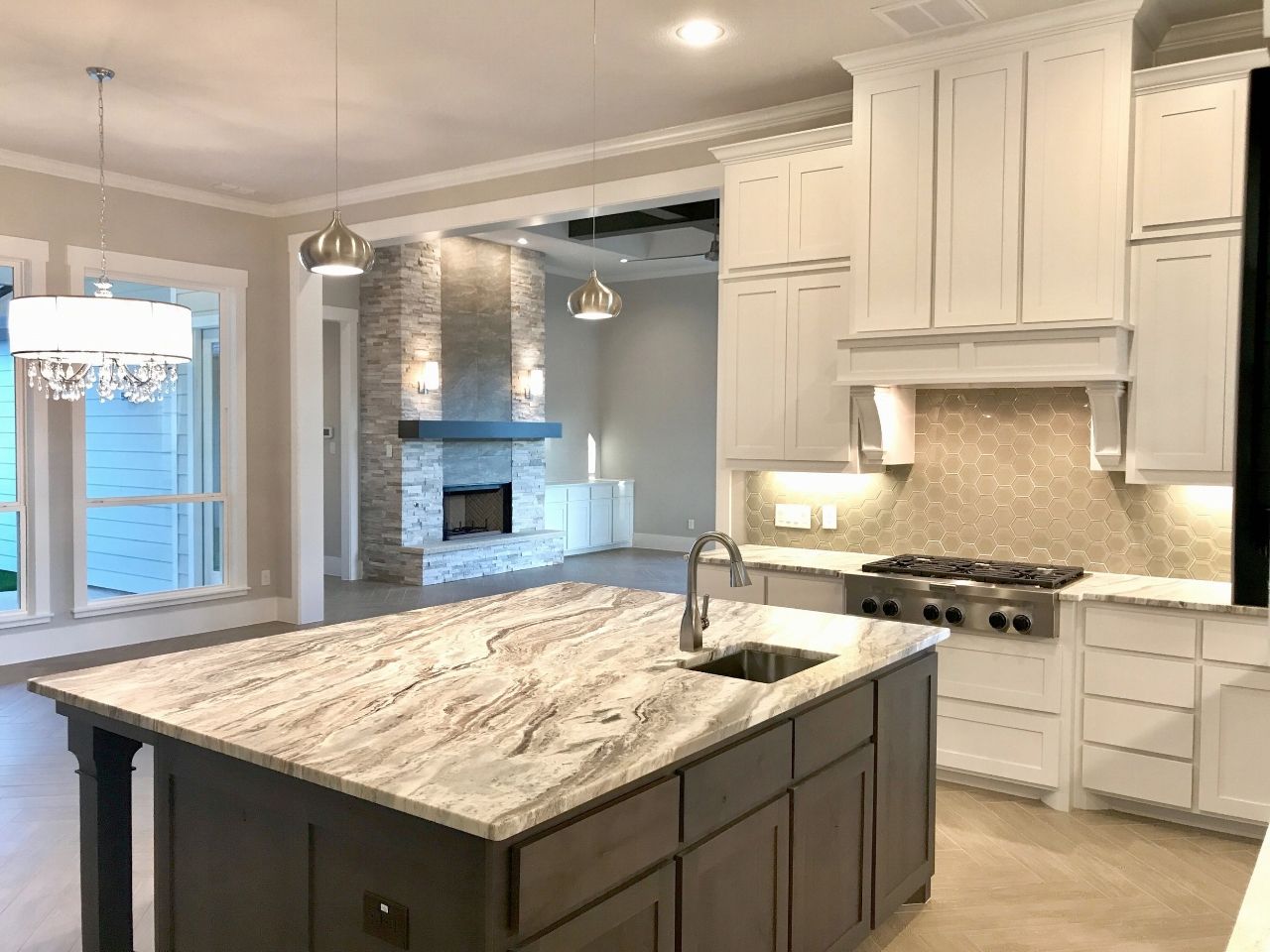 Kitchen with island and stove. Fireplace in background. White cabinets and light-colored countertops.