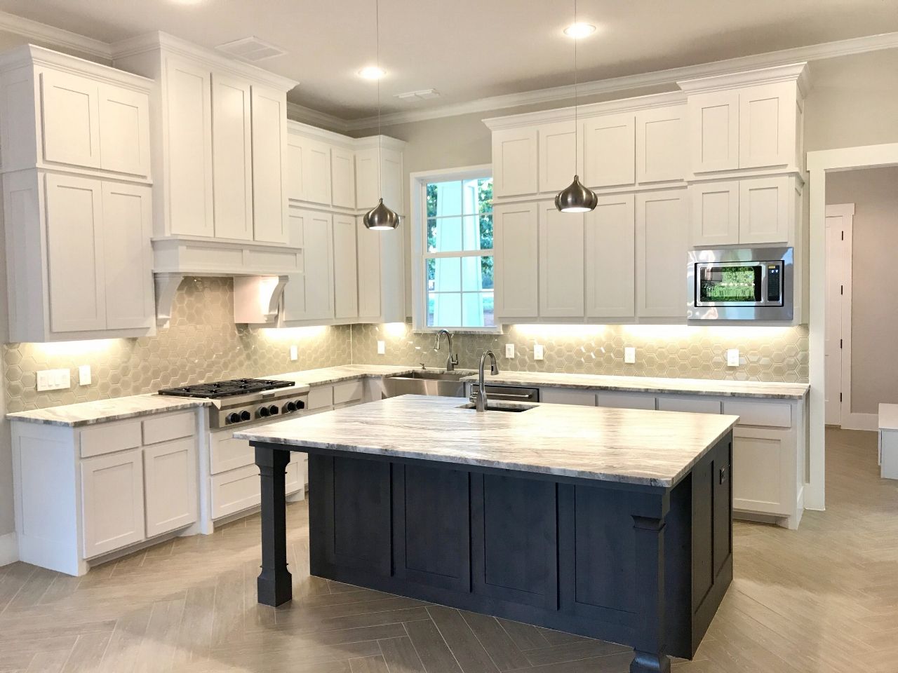 Kitchen with white cabinets, dark island, and stainless steel appliances.