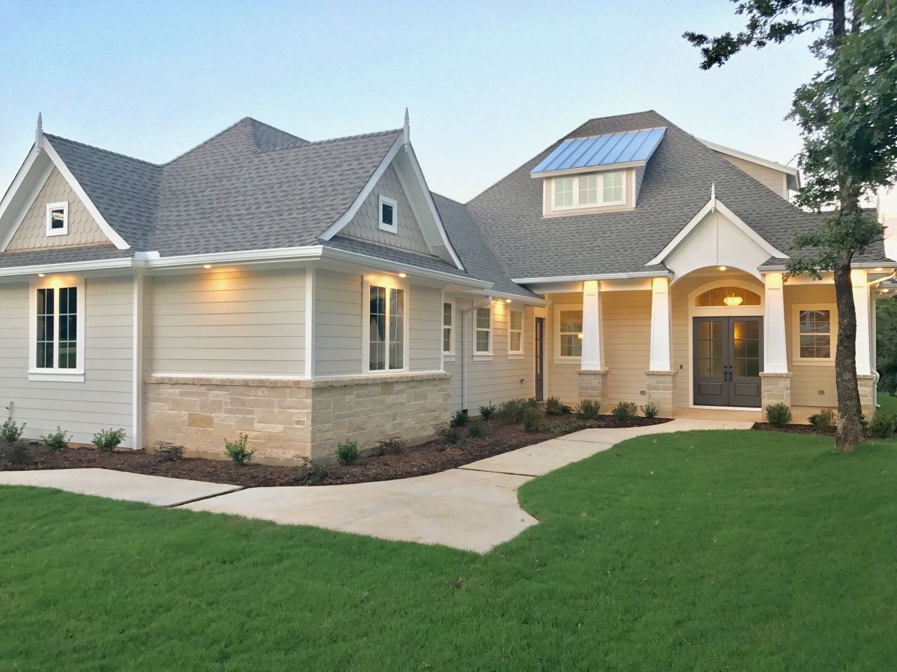 Light gray house with stone accents, a landscaped lawn, and a walkway leading to the front door.