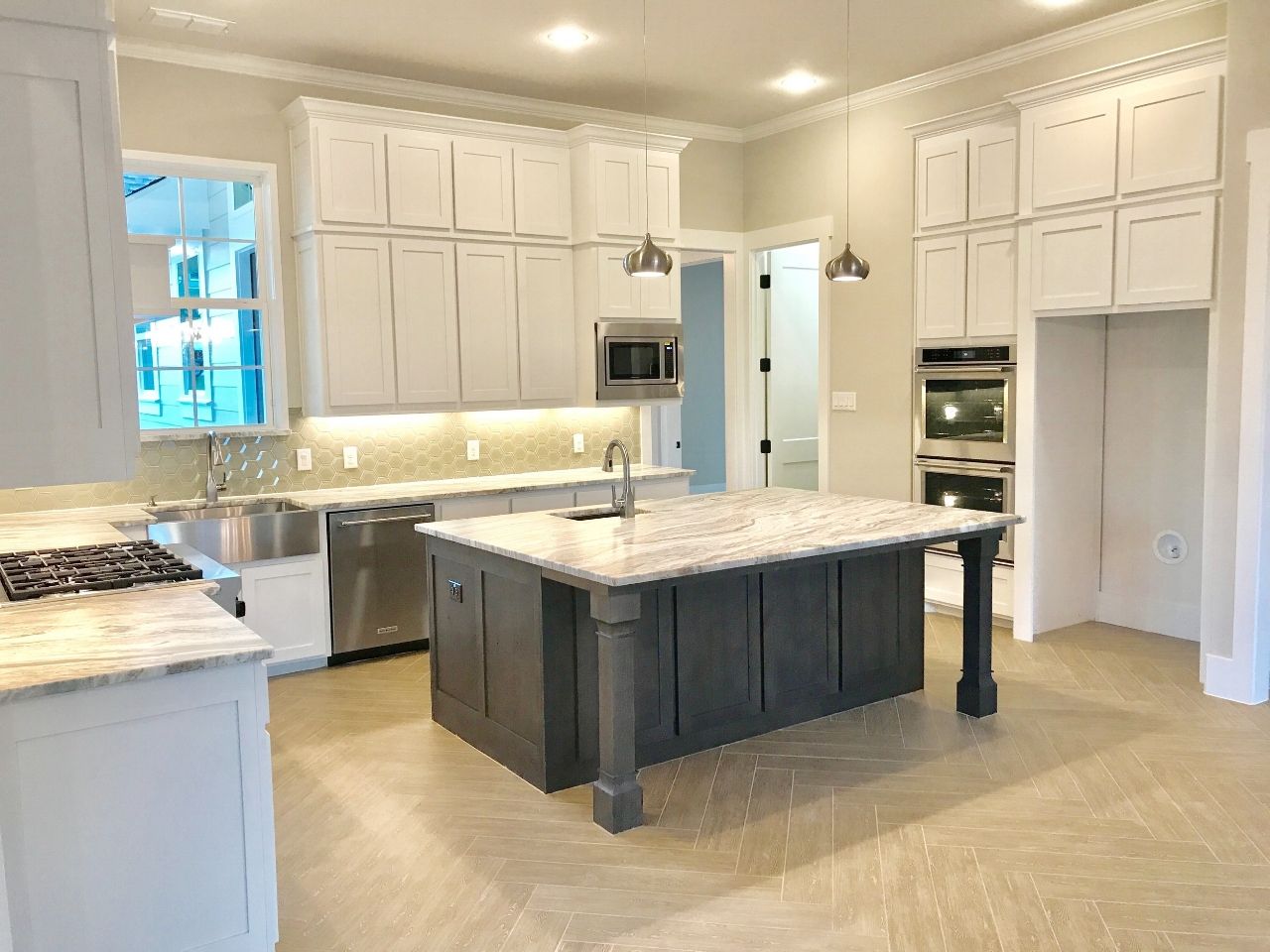 Spacious kitchen with white cabinets, gray island, stainless steel appliances, and beige flooring.