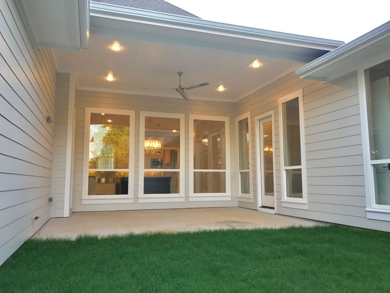 Patio of a house with windows, lights, and a ceiling fan, with green grass in the foreground.