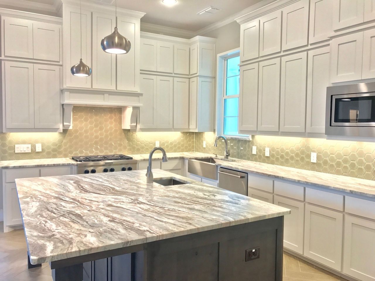 Modern kitchen with white cabinets, island, granite countertop, stainless steel appliances, and gold backsplash.