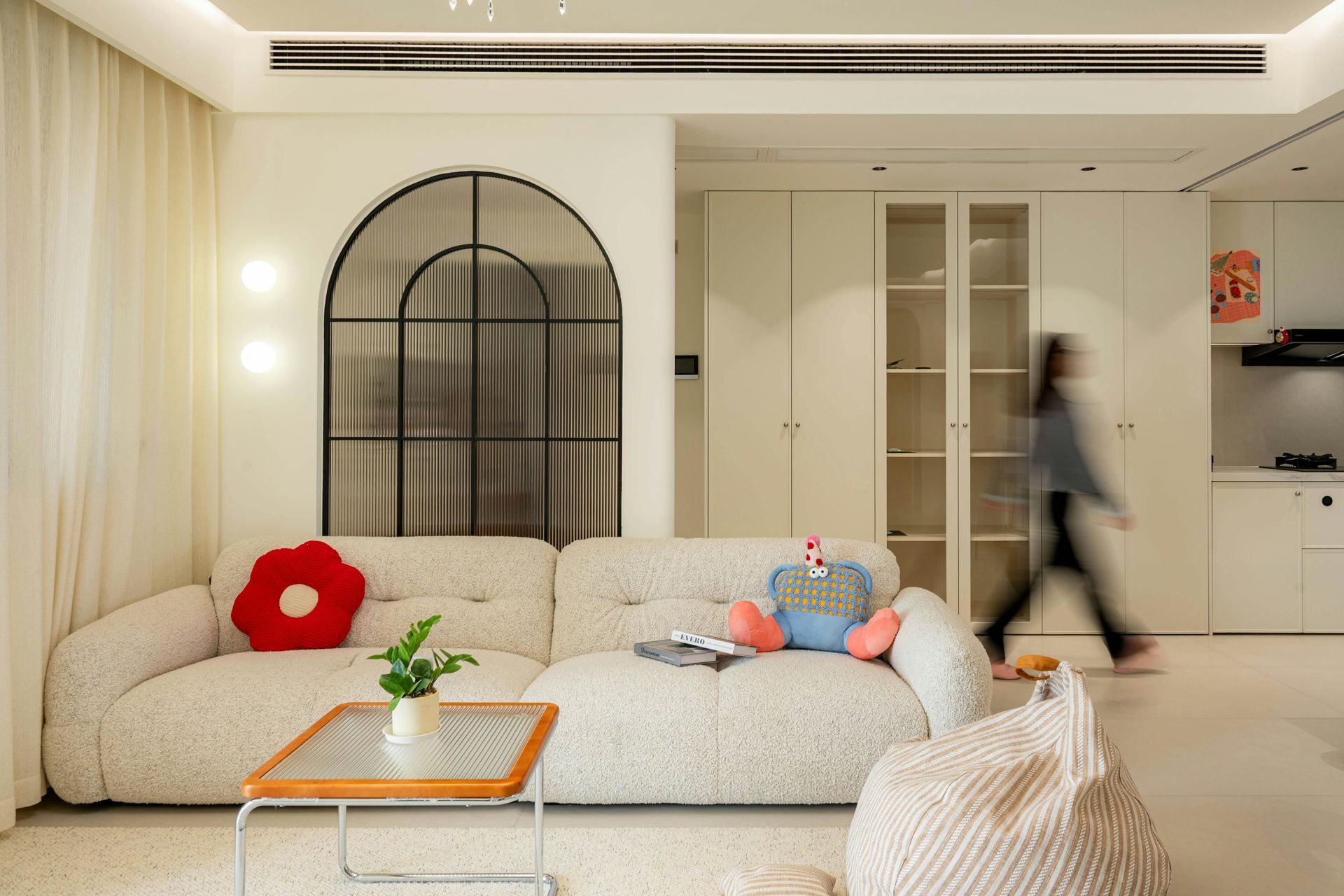 Living room with white sofa, arched window, and person walking.
