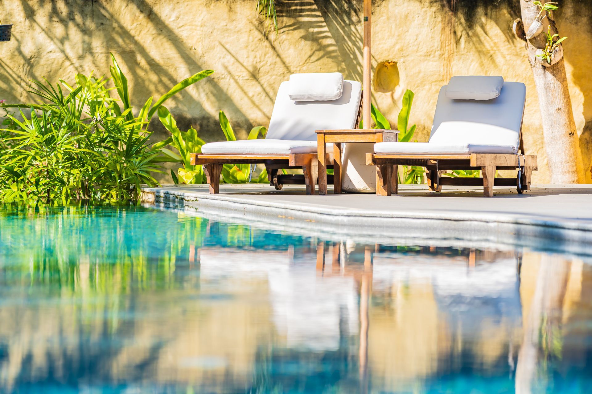 Two lounge chairs and a small table beside a pool in a sunny outdoor setting.
