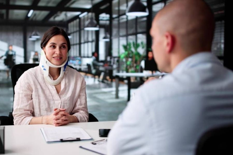 A person with their arm in a sling sits at a desk during a consultation with a healthcare professional.