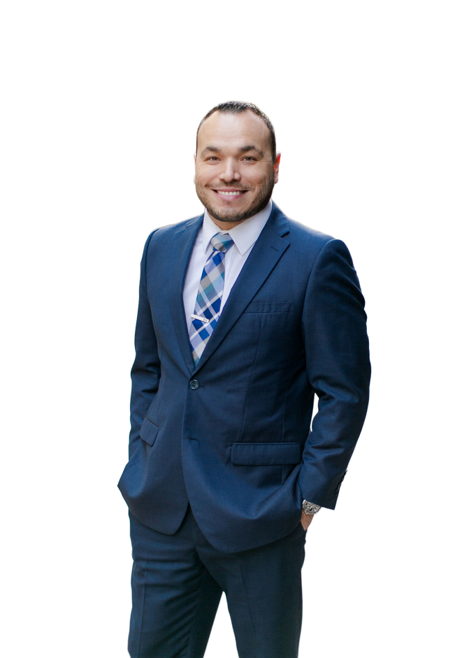 Smiling man in a blue suit and patterned tie, standing with hands in pockets against a white background