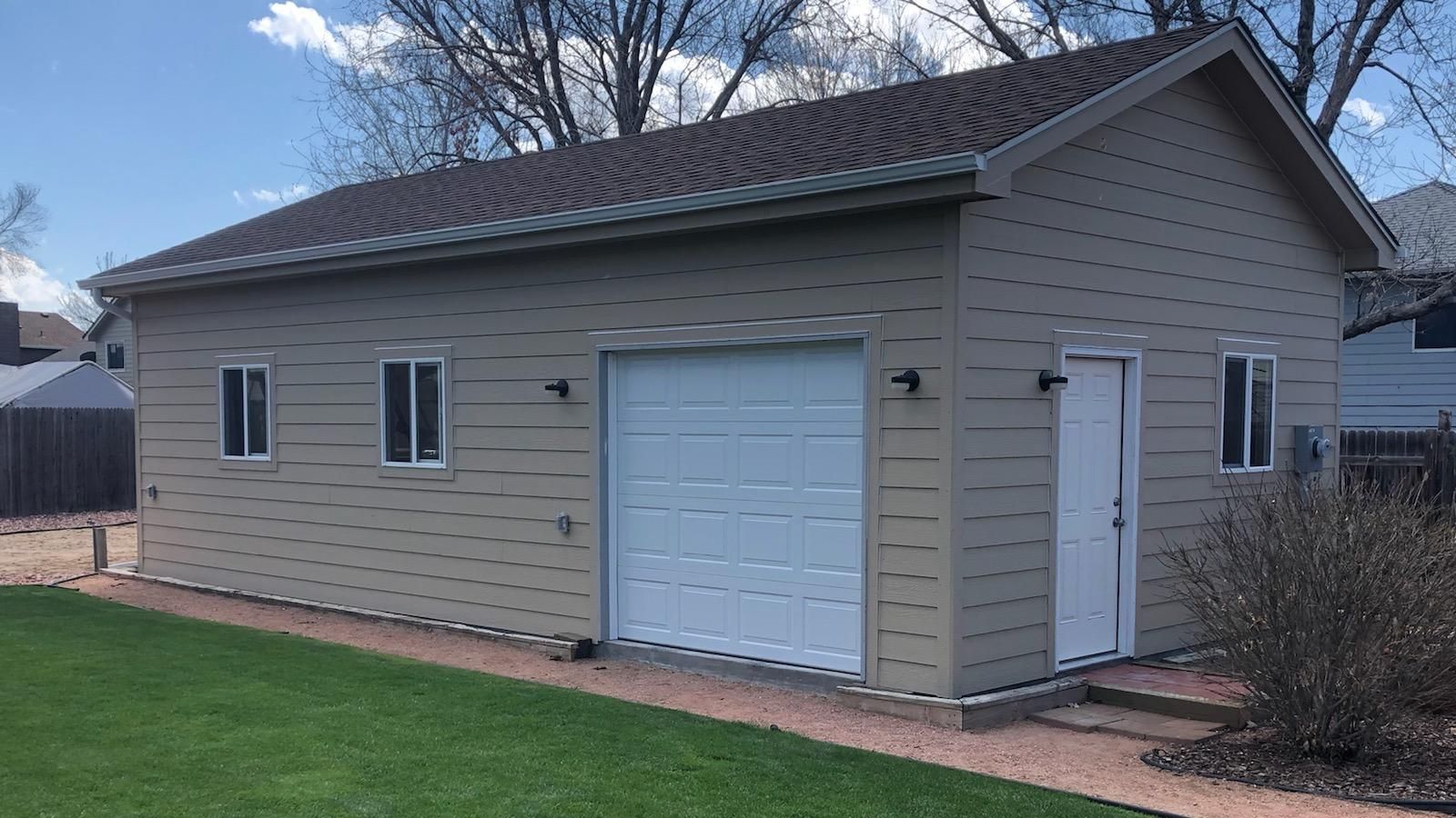 a garage with a white garage door and windows is in the backyard of a house .