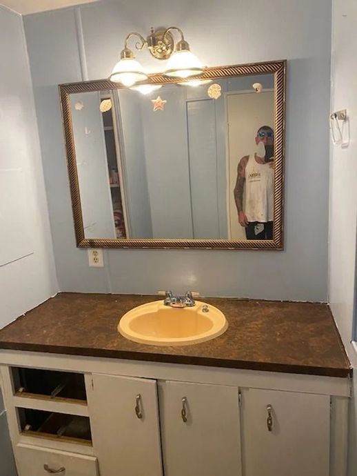 Bathroom vanity with brown countertop, round yellow sink, mirror, and wall light fixture.