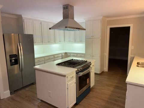 Modern kitchen with stainless steel appliances, white cabinets, and a central gas range.