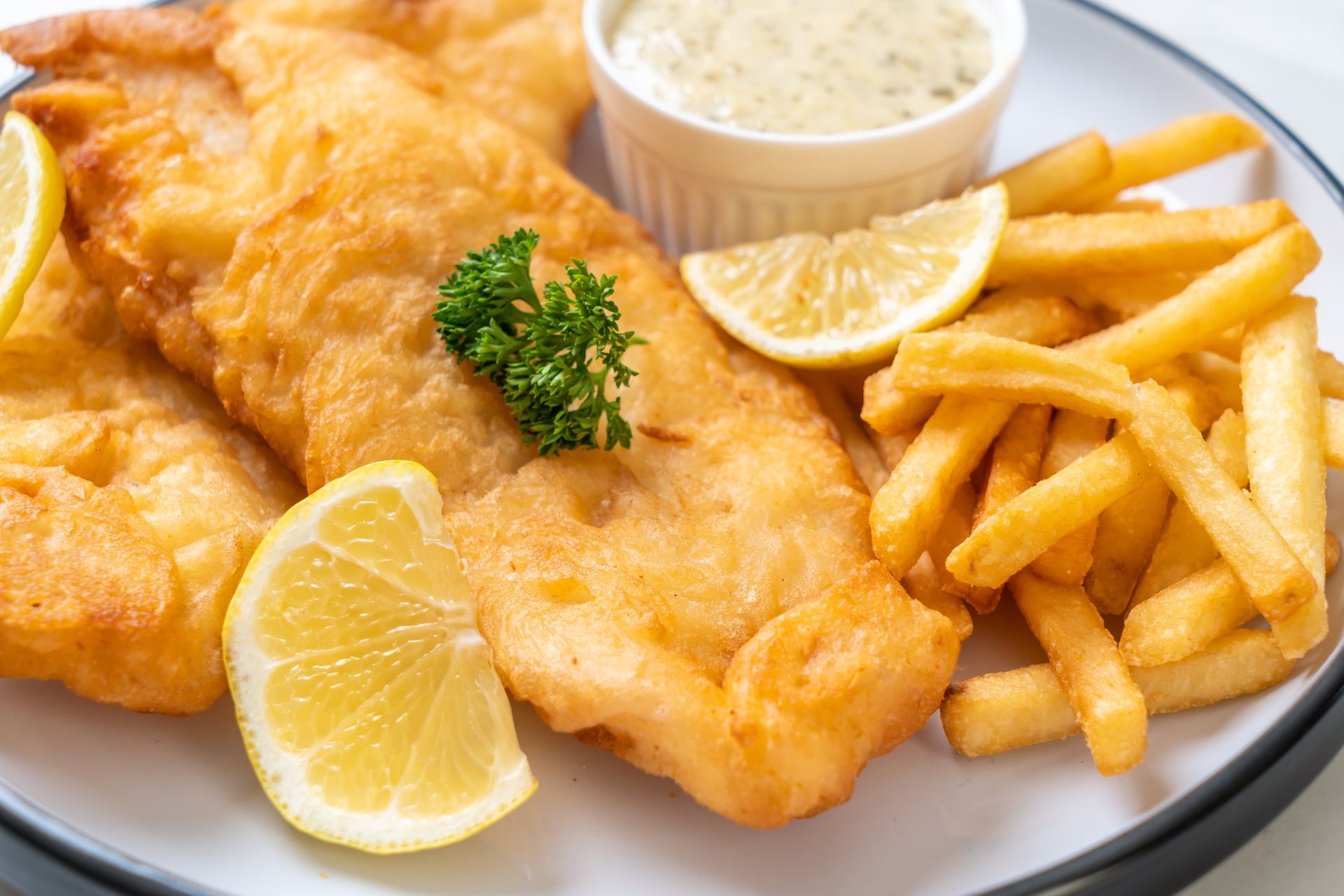 A plate of fish and chips with lemon slices on a table.