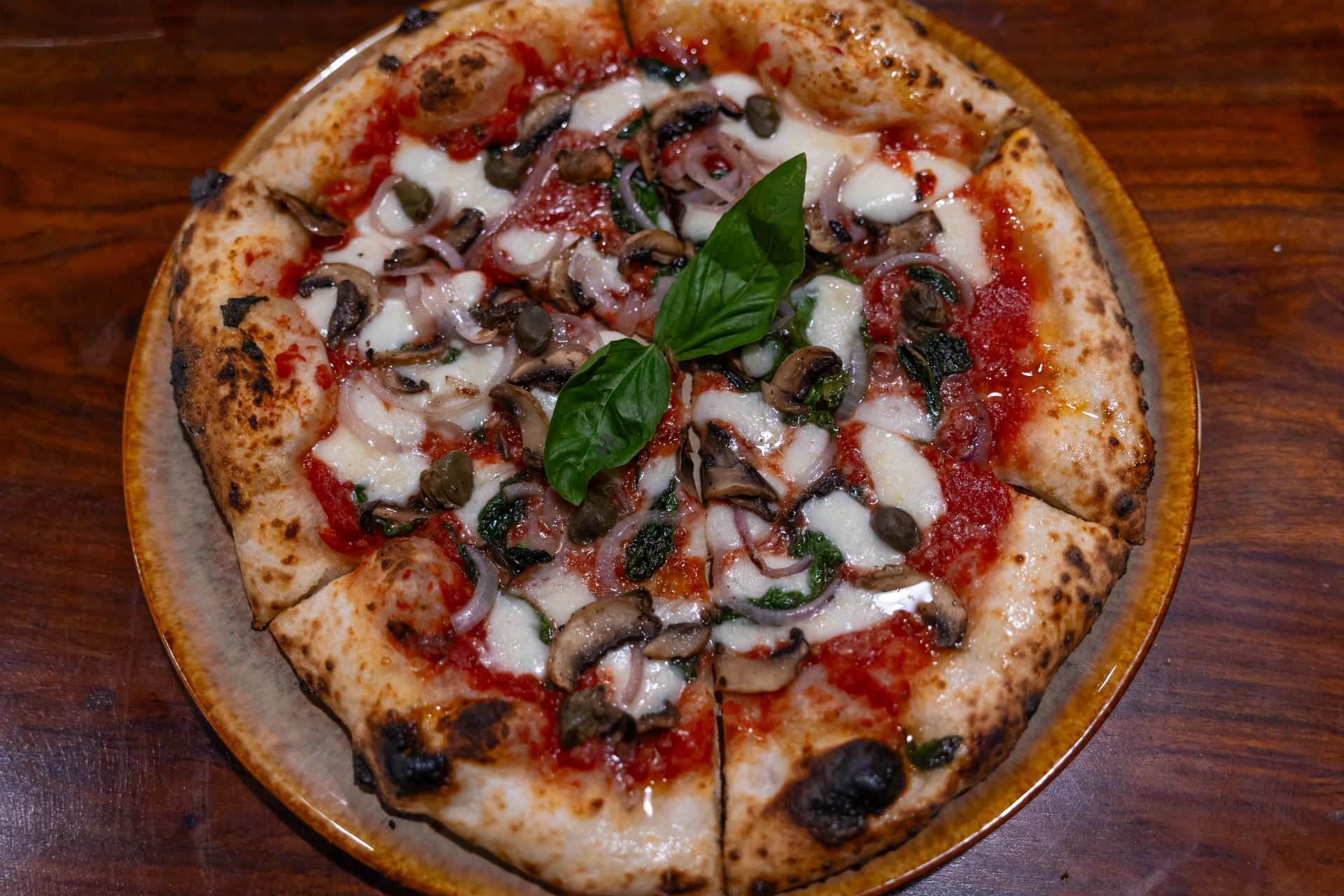 A pizza with mushrooms and basil on a plate on a wooden table.