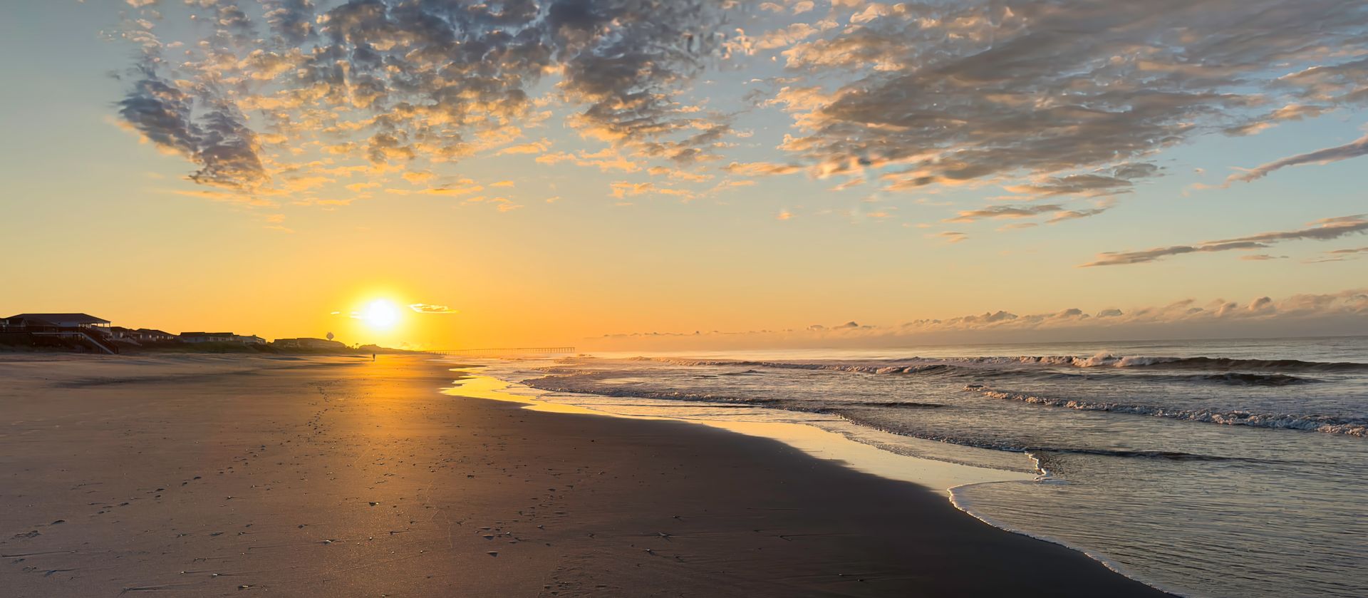 The sun is setting over the ocean on a beach.