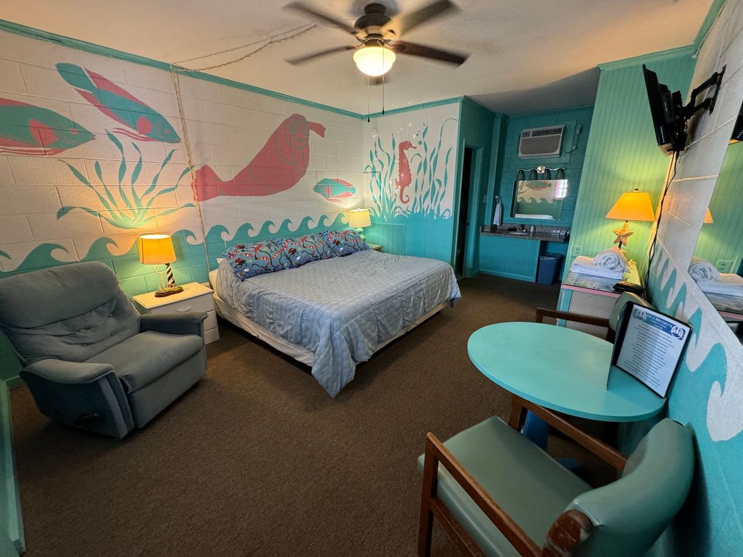 A hotel room with a bed , chair , table and ceiling fan.