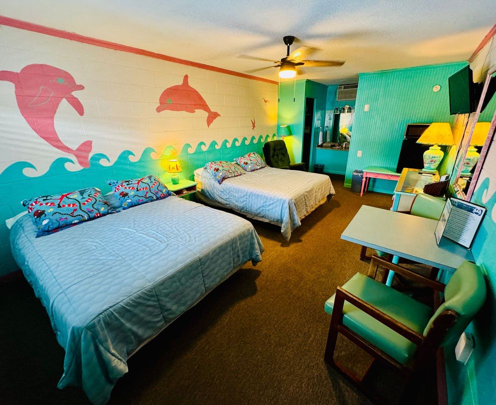 A hotel room with two beds and a desk with dolphins painted on the wall