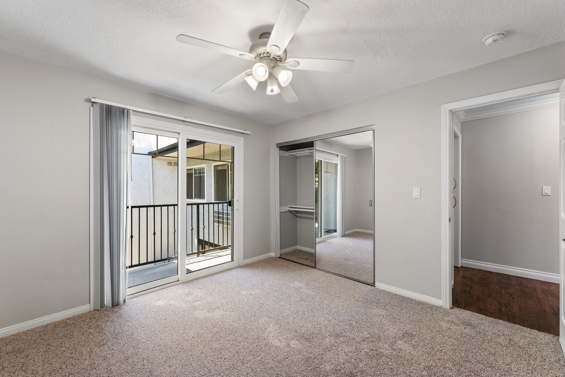 Carpeted bedroom with patio door and glass mirrored sliding closet