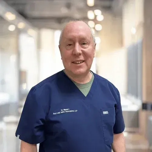 A professional in dark blue medical scrubs smiling in a bright, modern office hallway.