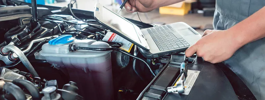 A mechanic uses a laptop and a probe to diagnose a car engine in a garage.