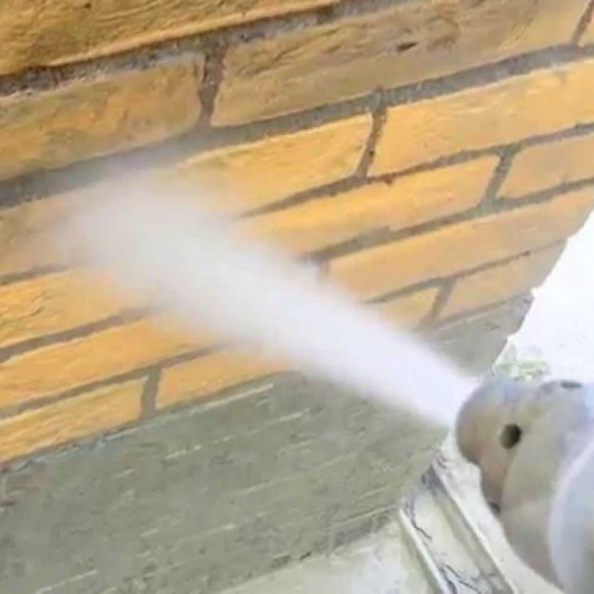 A person is spraying water on a brick wall.