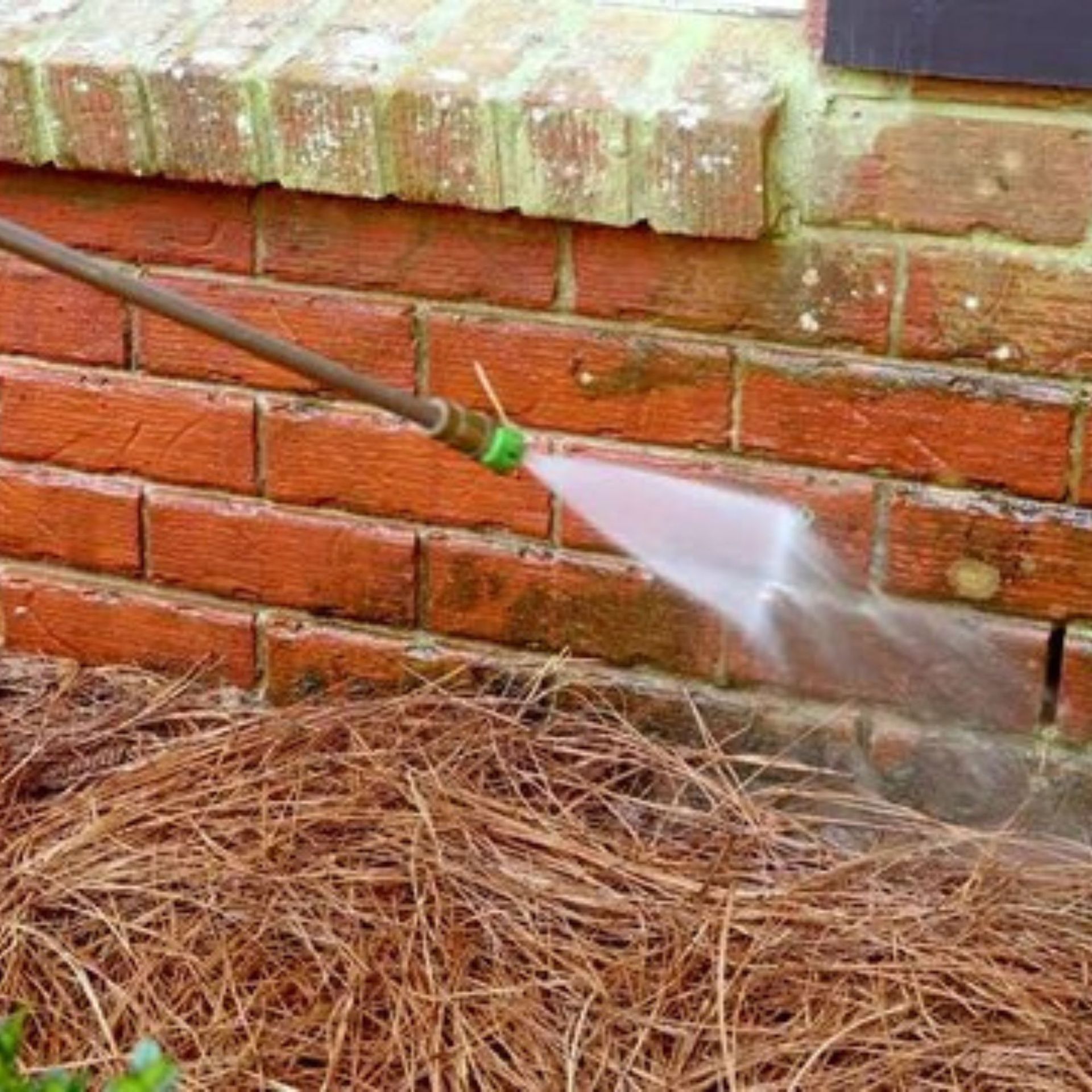 A person is spraying a brick wall with a hose.