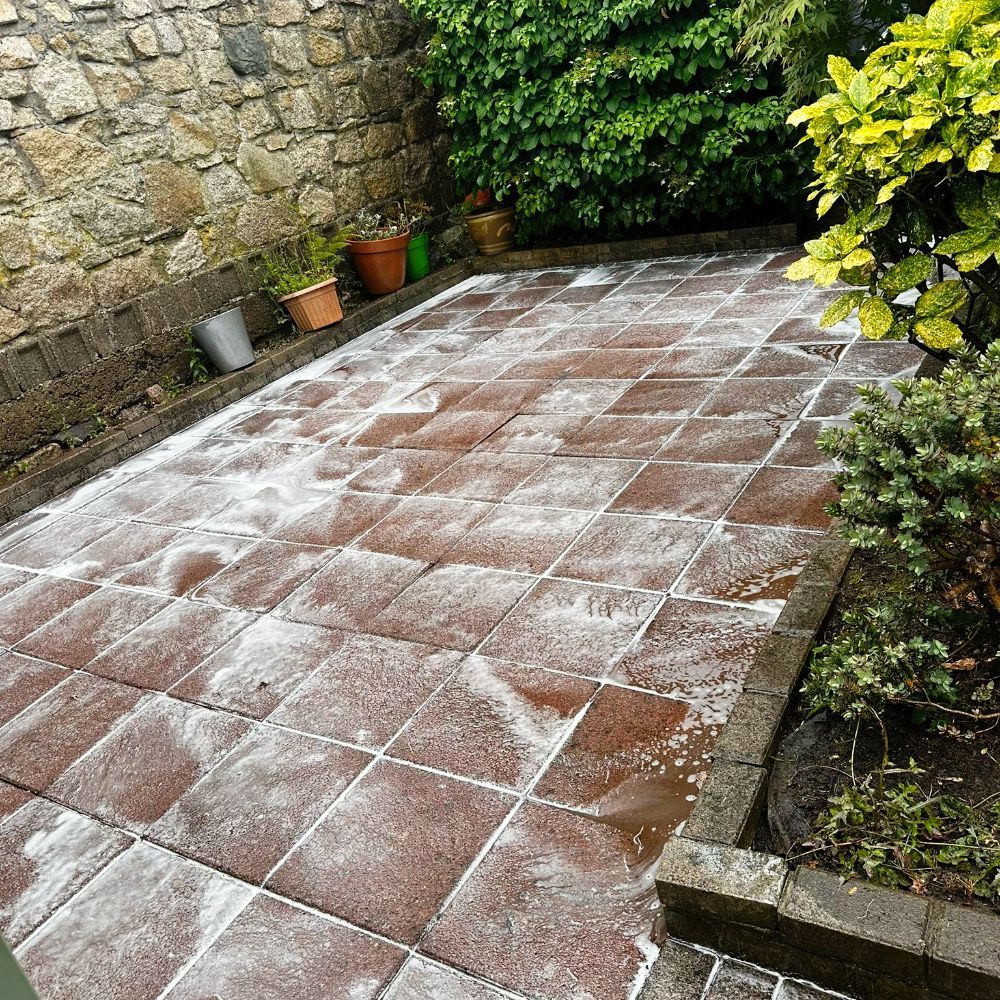 A patio with a lot of tiles and plants in the background.