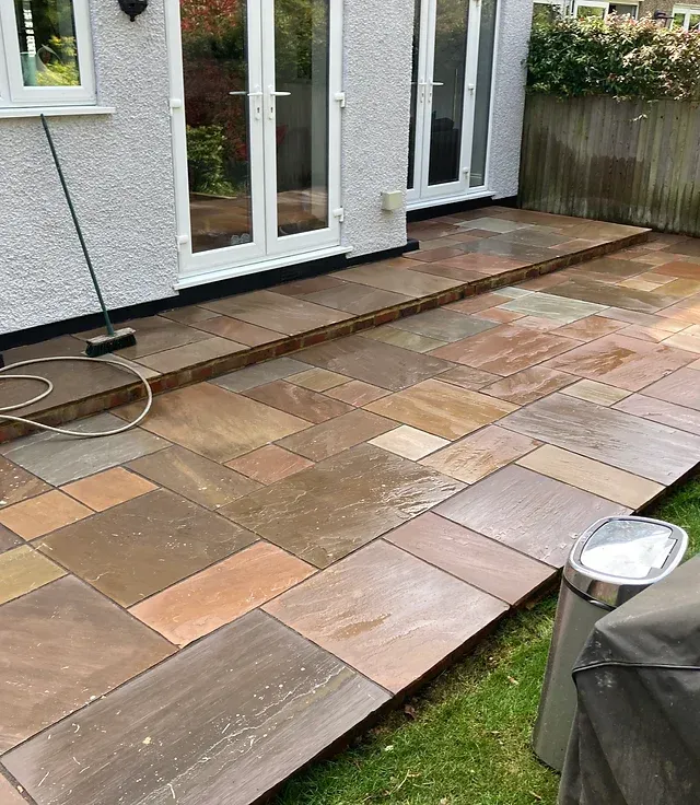 A patio with a broom and a trash can in front of a house.