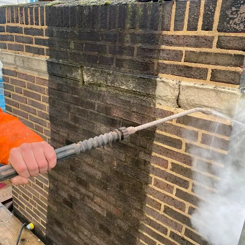 A person is cleaning a brick wall with a high pressure washer.