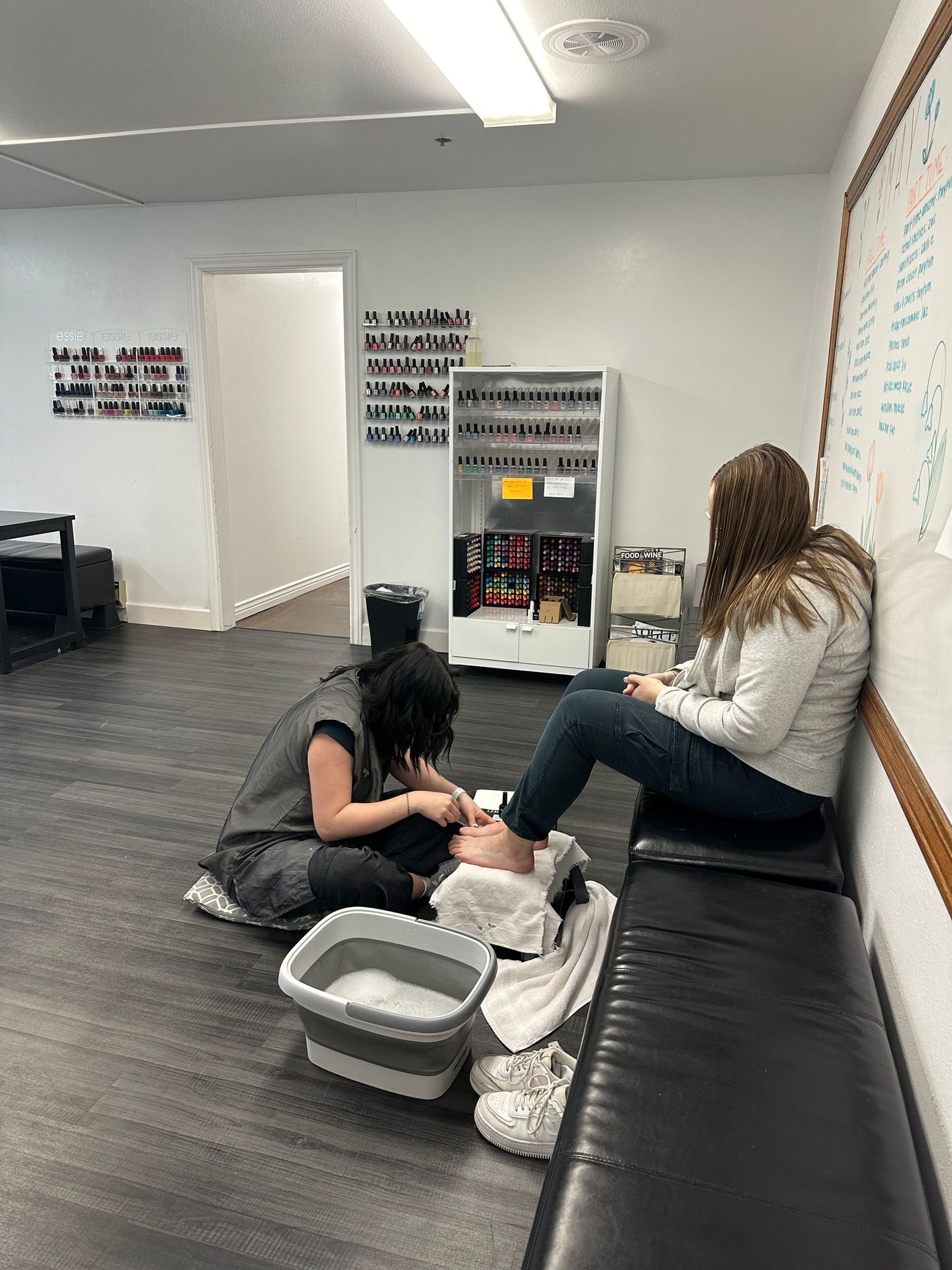 Two women are sitting on a couch in a room getting their feet washed.