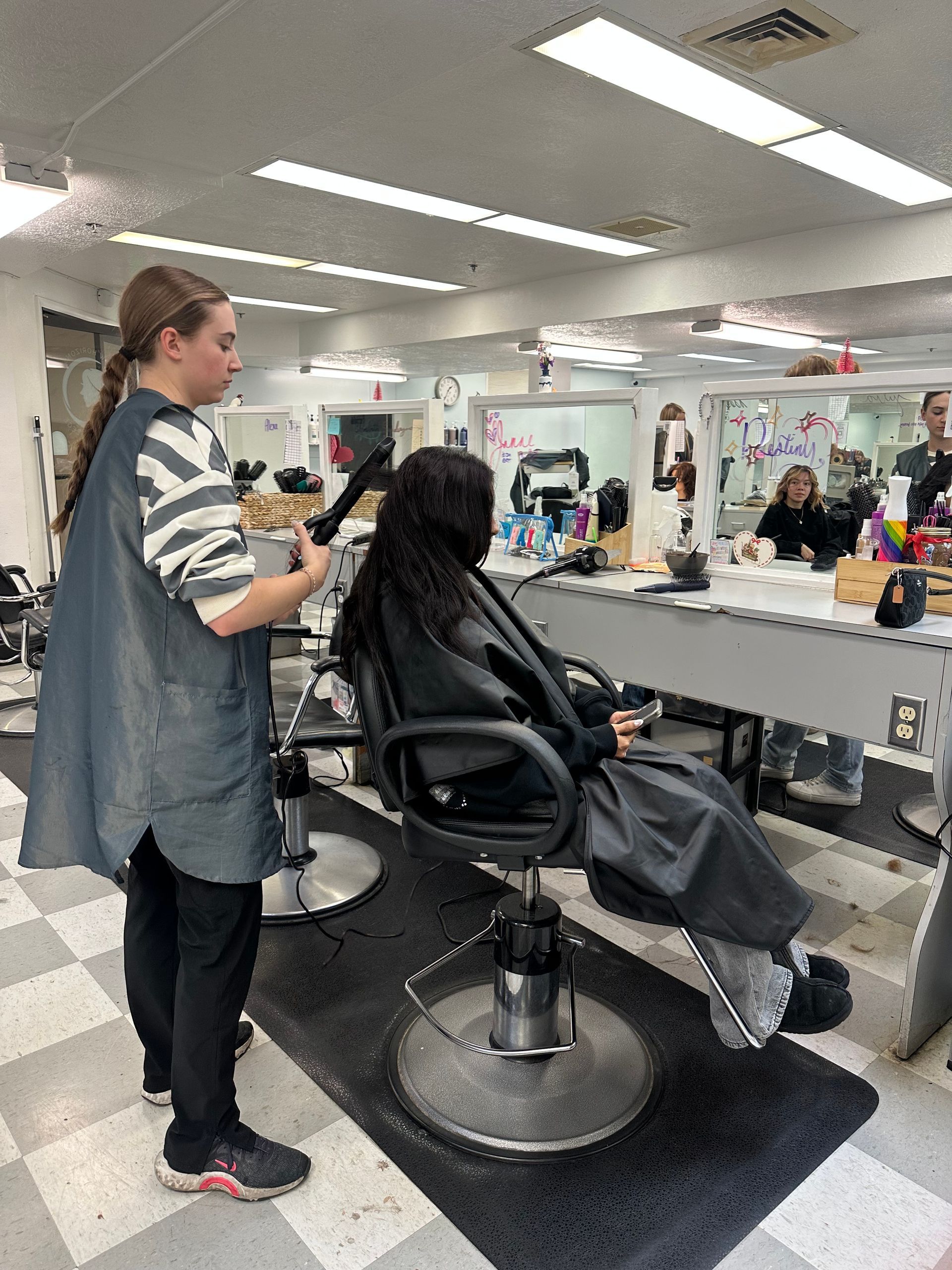 A person stands behind a salon chair, styling a client's hair in a brightly lit hair salon. A person stands behind a salon chair, styling a client's hair in a brightly lit hair salon.