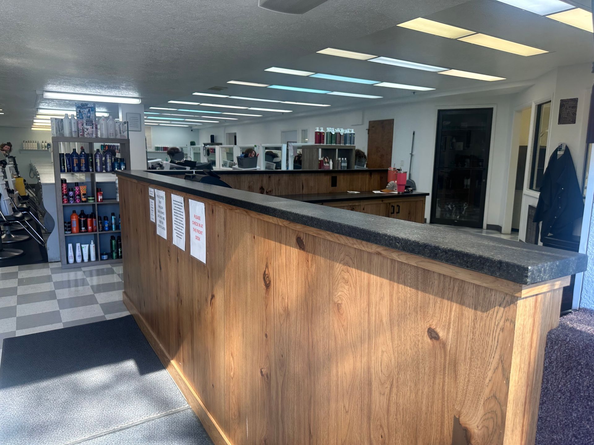 A wooden reception desk in a brightly lit business interior, with product shelves and a tiled floor in the background.