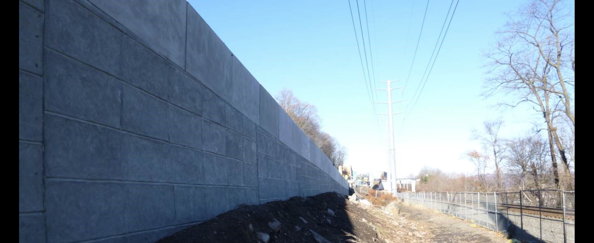 A large concrete wall is surrounded by trees and power lines.