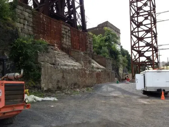 A white trailer is parked in front of a rusty bridge