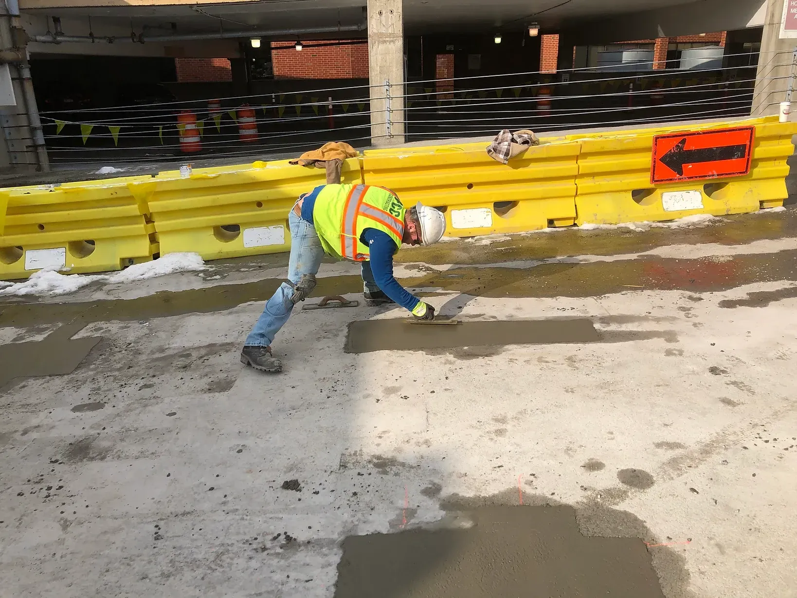 A man in a safety vest is laying concrete on the ground