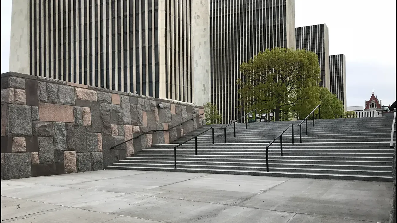 A person is riding a skateboard down a set of stairs in front of a building.