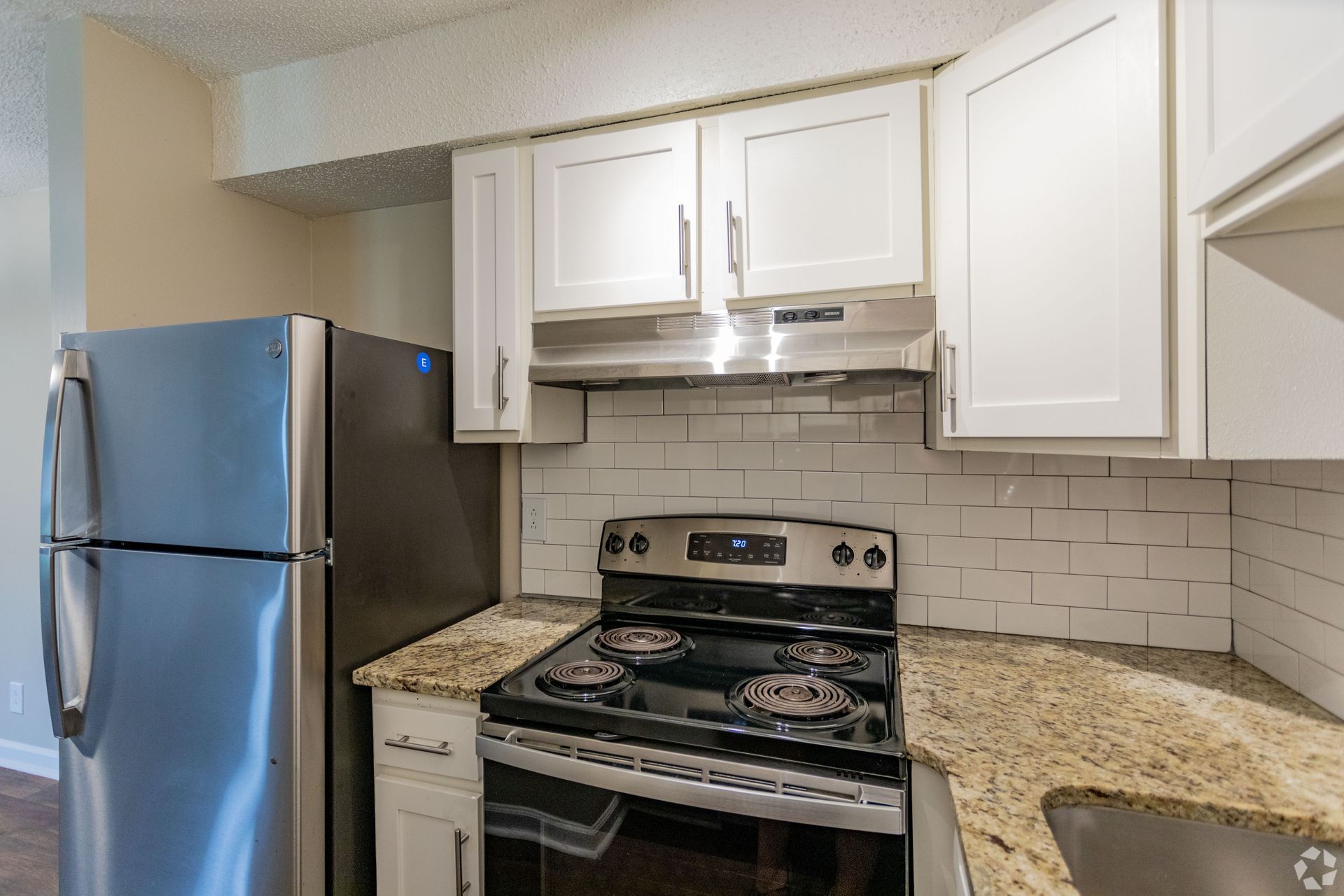 A kitchen with white cabinets, speckled granite countertops, a subway tile backsplash, and stainless steel appliances.