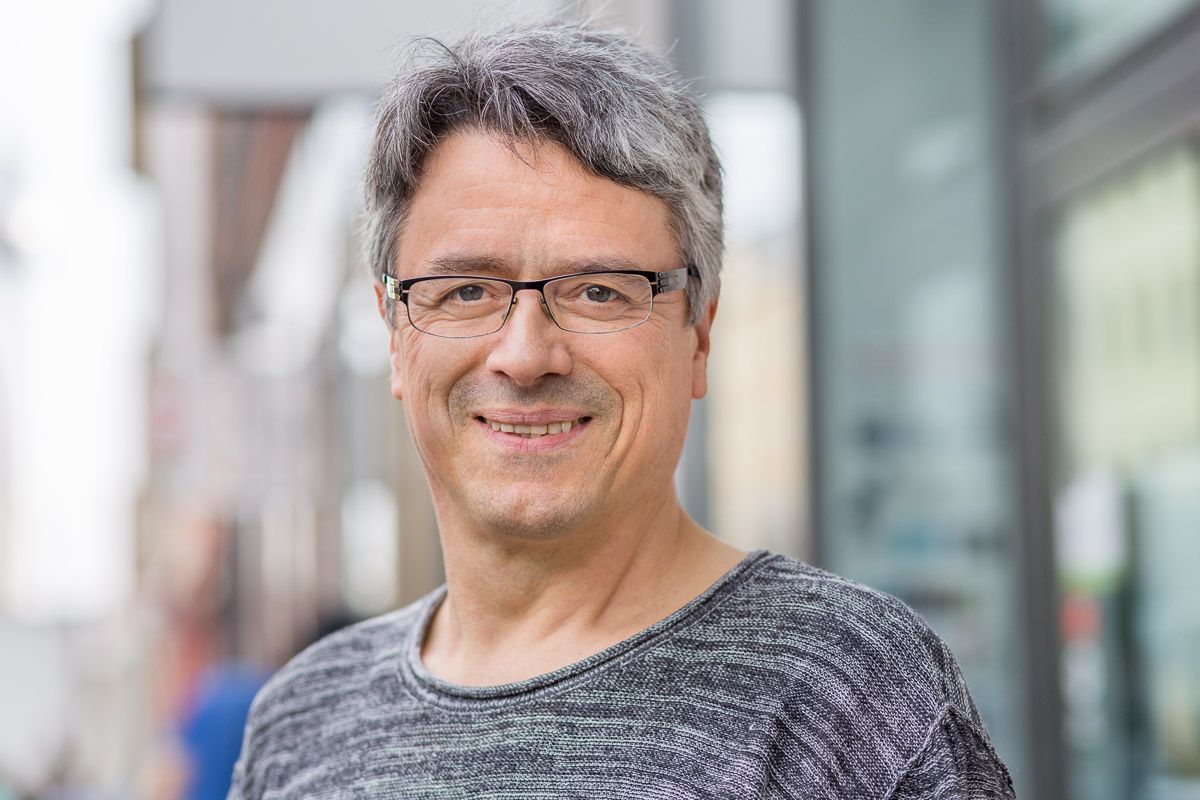 Ein Mann mit Brille und grauem Hemd lächelt in die Kamera.