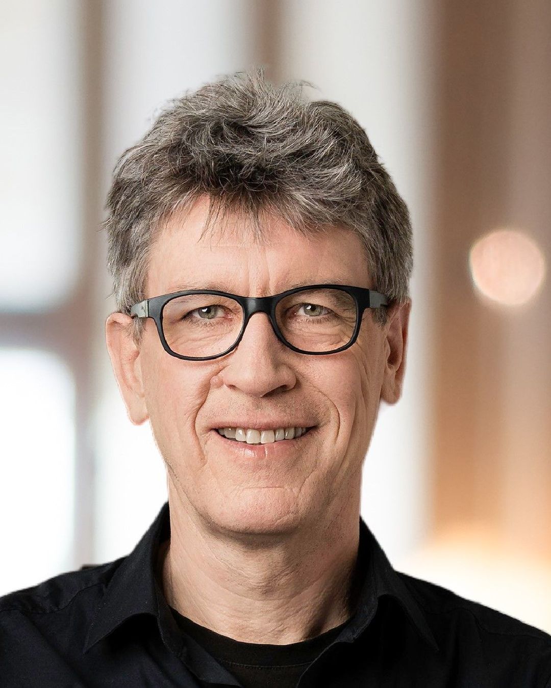 Ein Mann mit Brille und schwarzem Hemd lächelt in die Kamera.