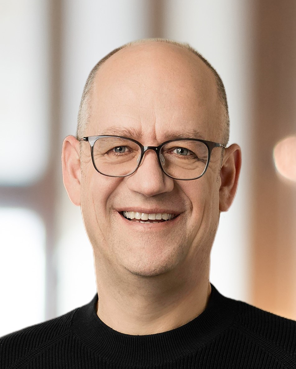 Ein kahlköpfiger Mann mit Brille und schwarzem Hemd lächelt in die Kamera.