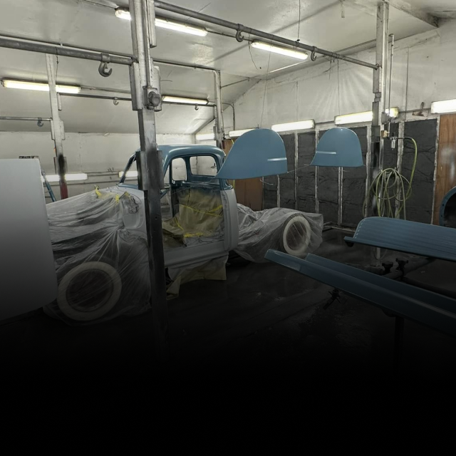 A vintage truck in a paint booth being prepped for paint. Blue car parts and white tires are visible. | Alex’s Paint & Body