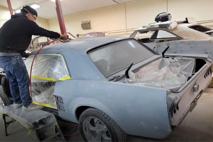 A person spraying primer on a classic car in a body shop. | Alex Paint Body