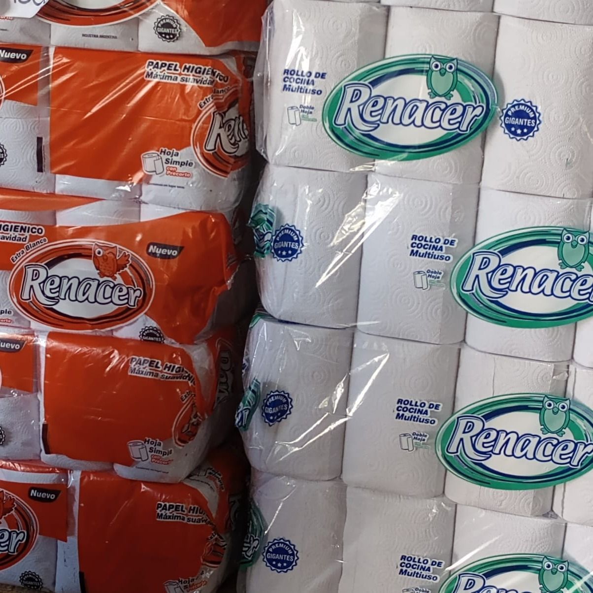 Montones de toallas de papel marca Renacer en empaques blancos y naranjas, listas para la venta.